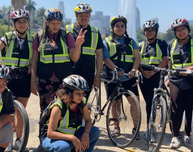 Cyclists in black vests with high visibility stripes posing with their bikes informant of the fountain at Echo Park Lake.